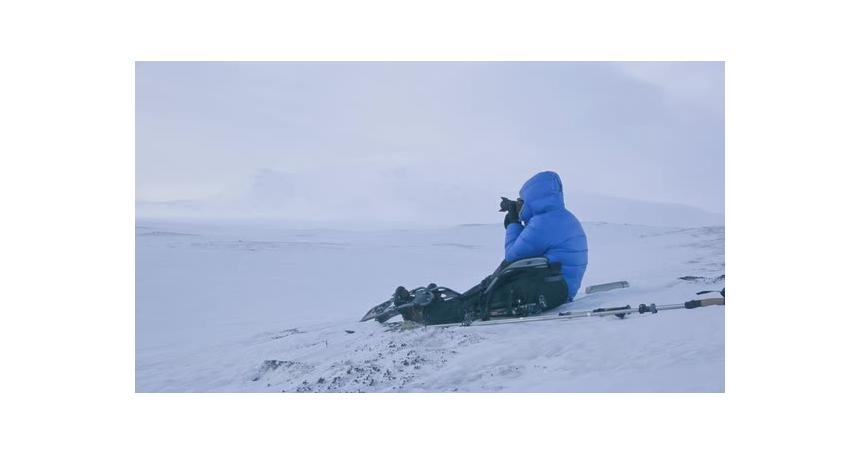 A tourist in a blue jacket takes pictures of snow-covered mountains in Norway.