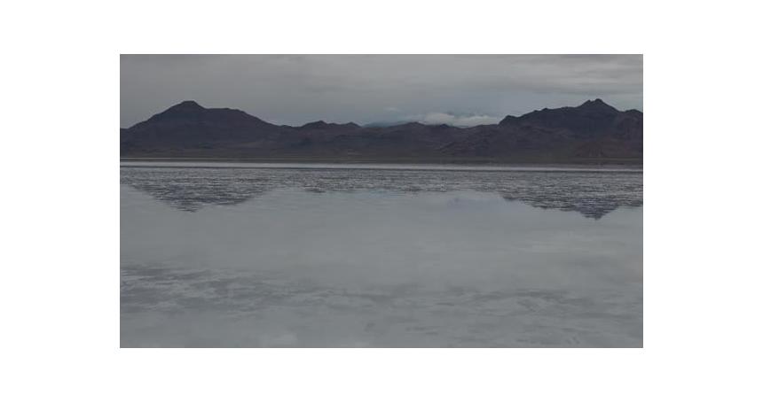 Drone slow low approach over Bonneville Salt Flats with water reflecting the sky and clouds with mou