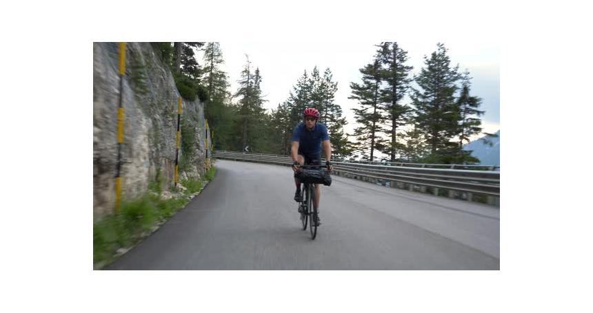 Male Caucasian model Cycling on the open road down hill in a mountain area next to a cliff, Dolimite