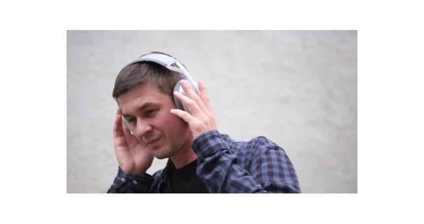 Young Man in Blue Checkered Shirt and Black Tshirt Listens to Music with Large White Headphones and